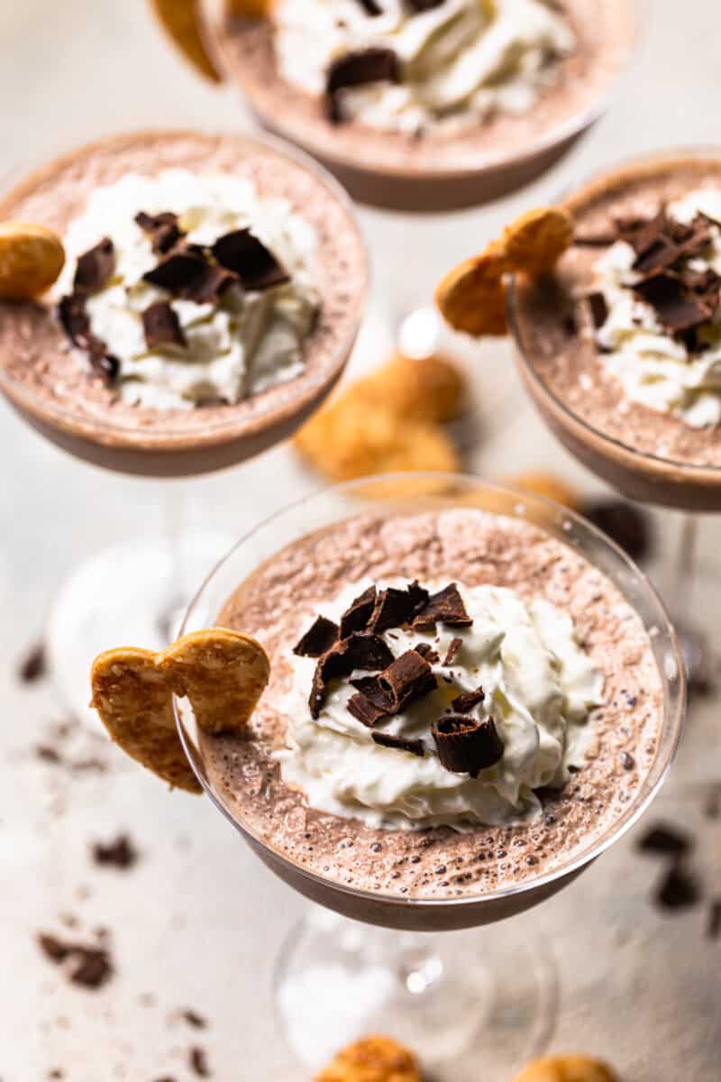 frozen french silk pie cocktails in glasses topped with whipped surf and chocolate shavings and garnished with baked pie husks cookies