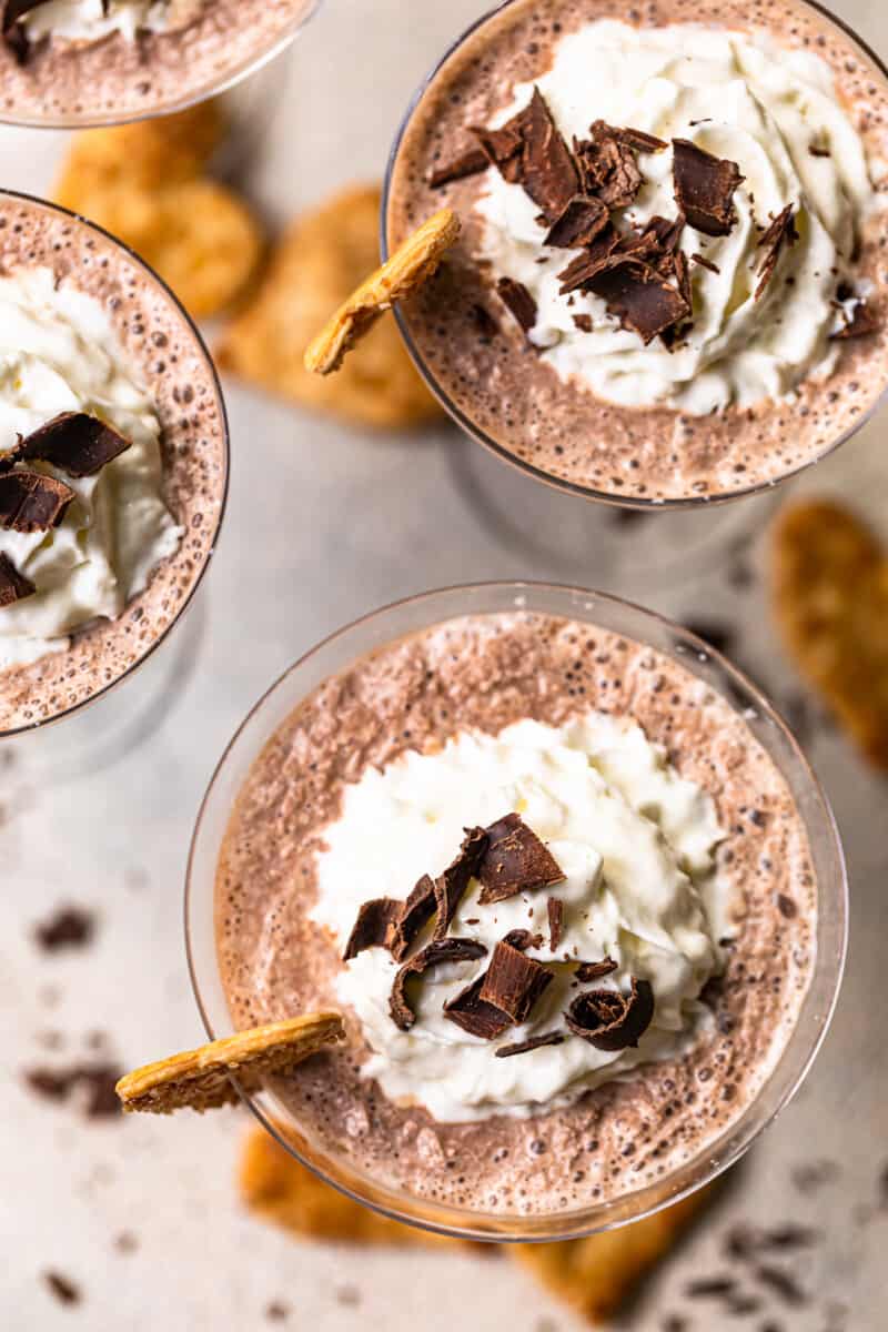 overhead image of frozen french silk pie cocktails in glasses topped with whipped surf and chocolate shavings and garnished with baked pie husks cookies