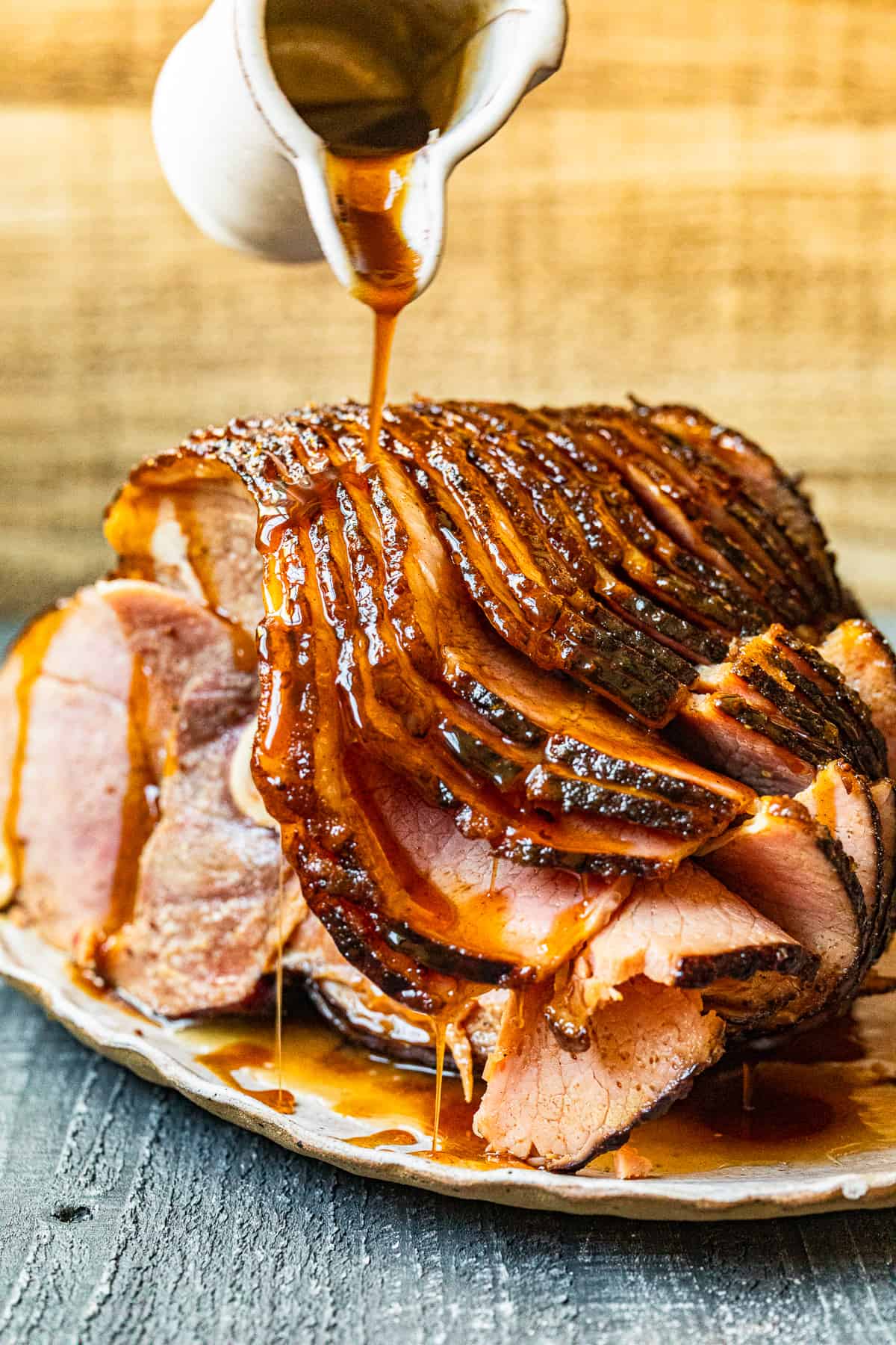 hand pouring glaze onto honey baked ham on a white serving platter