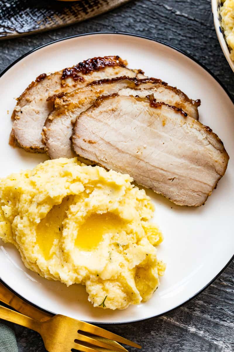 slices of honey baked pork tenderloin with mashed potatoes on a dinner plate
