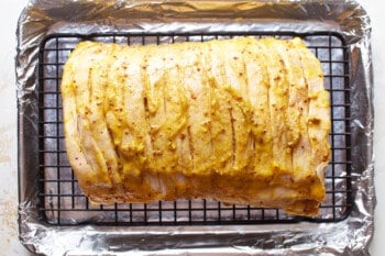 scored pork tenderloin with mustard glaze on a wire rack set in a baking sheet.