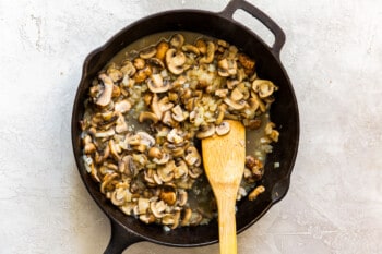 mushrooms and onions with wine in a skillet with a wood spoon