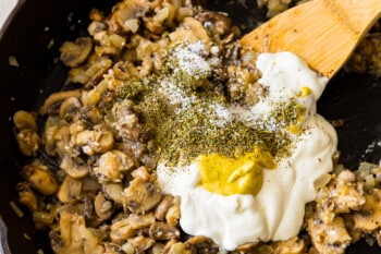 cooked mushrooms and onions with sour cream and spices in a skillet with a wood spoon