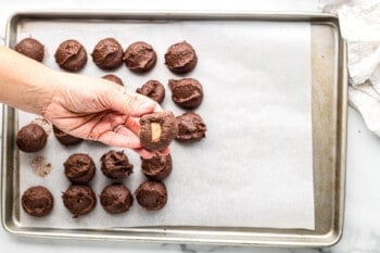 hand with a scoop of brownie cookie dough with a caramel stuffed inside covering the caramel