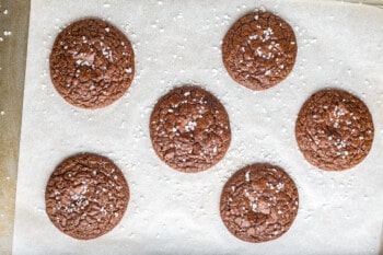brownie cookies topped with sea salt on a parchment paper lined baking sheet