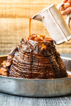 hand pouring glaze onto honey baked ham