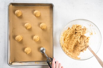 hand scooping oatmeal cookie dough onto a parchment paper lined baking sheet before baking