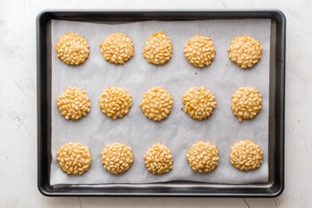 15 pignoli cookies on a parchment paper lined baking sheet