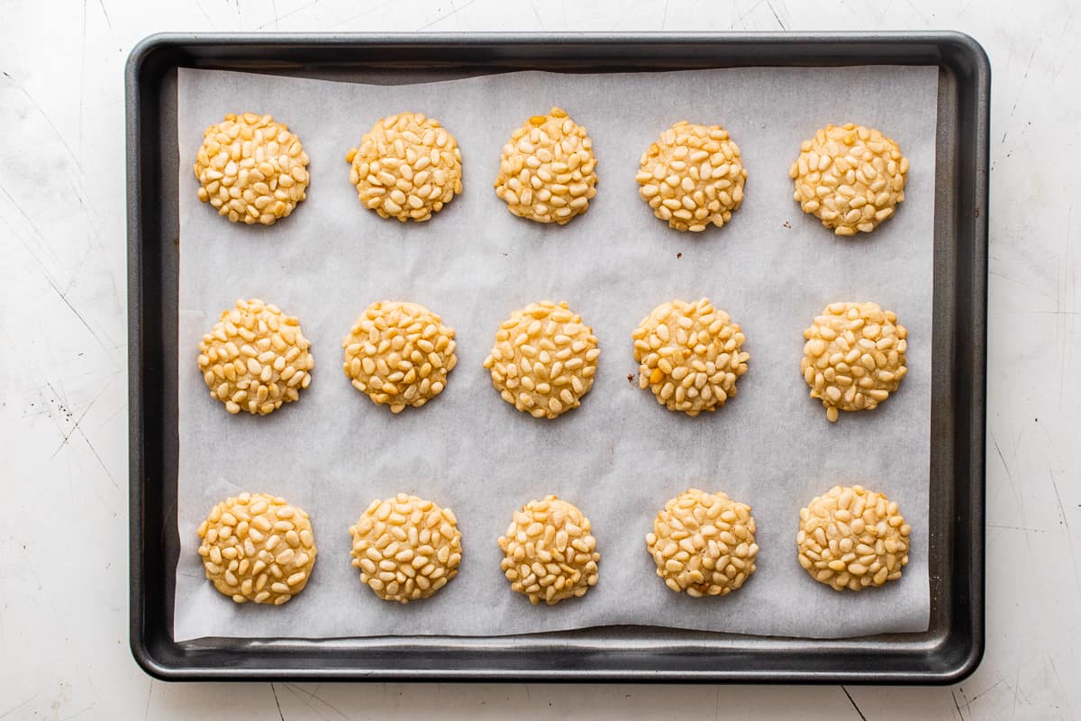 15 pignoli cookies on a parchment paper lined baking sheet