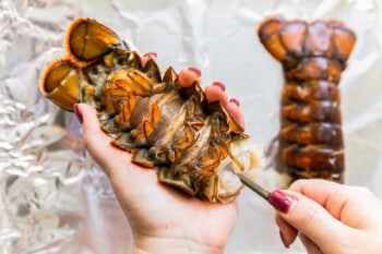 hand using a spoon to loosen the lobster tail meet