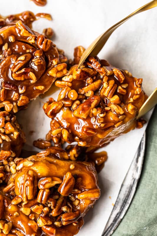 tongs grabbing a sticky bun off of a white serving tray