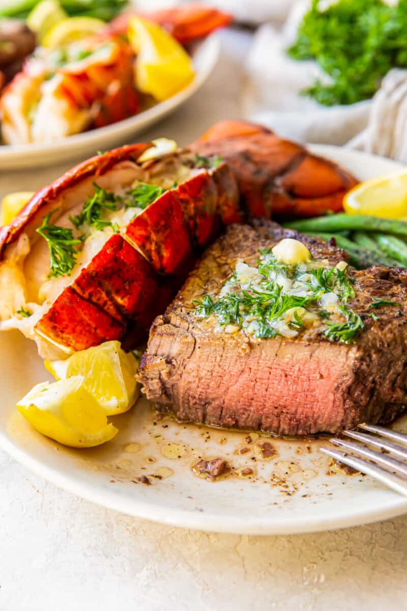 lobster tail and filet mignon with green beans on a plate with a fork