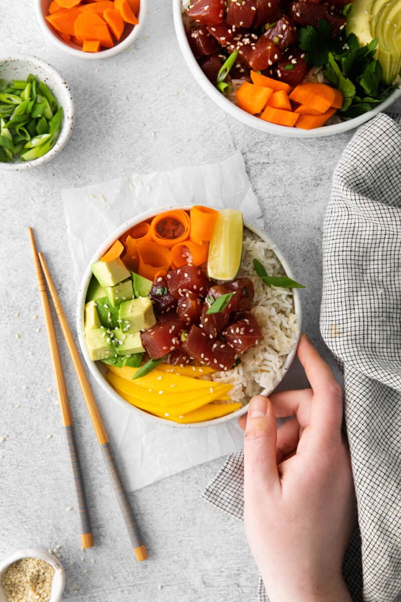 hand holding a tuna poke bowl in a white bowl with chopsticks.