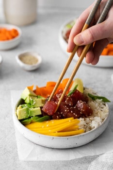 chopsticks grabbing a cube of tuna from a tuna poke bowl in a white bowl.