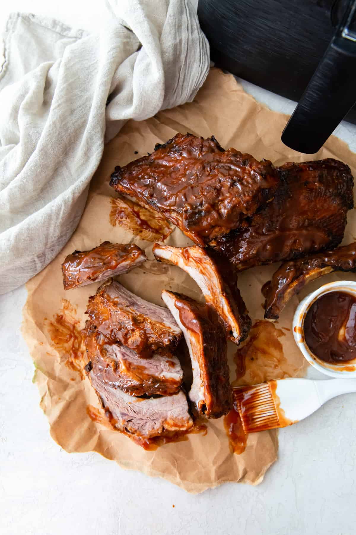 bbq ribs on parchment paper with a kitchen brush and bbq sauce in a bowl