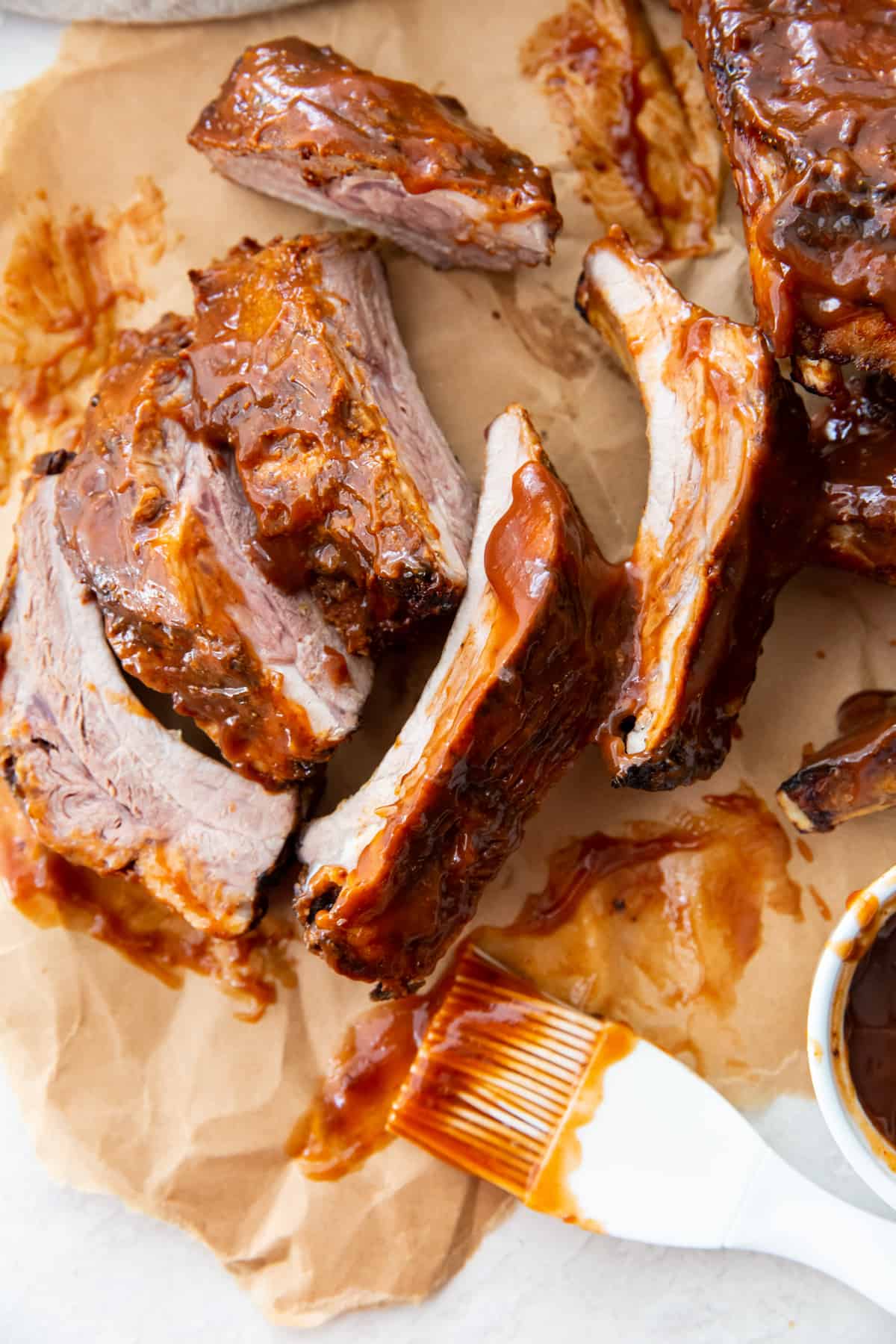 bbq ribs on parchment paper with a kitchen brush and bbq sauce in a bowl