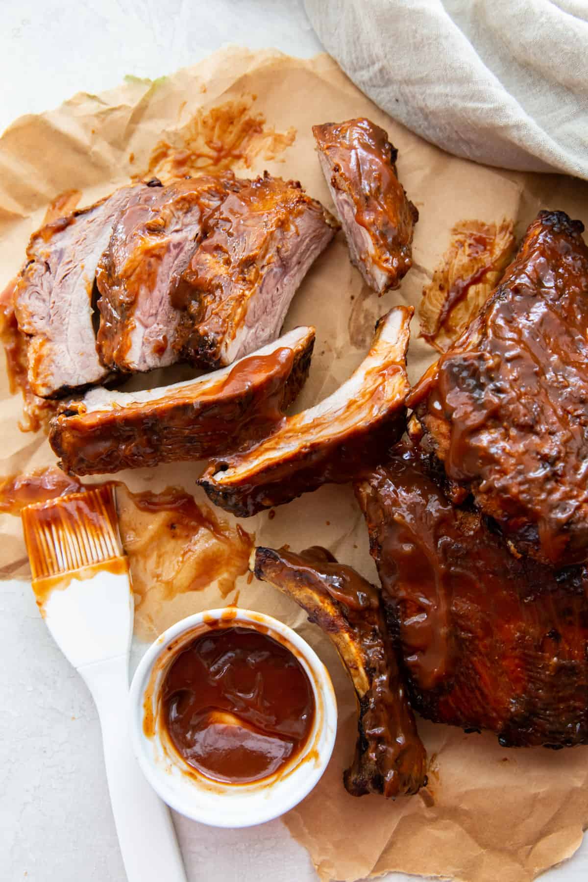 bbq ribs on parchment paper with a kitchen brush and bbq sauce in a bowl