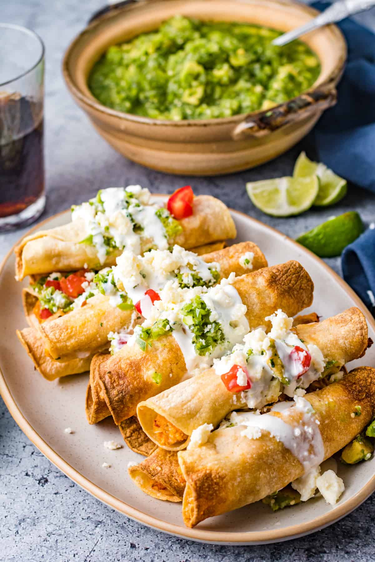 chicken taquitos on a serving plate topped with crema, guacamole, and diced tomatoes