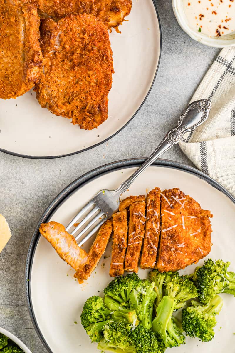 sliced pork chop and broccoli on a white plate with a fork