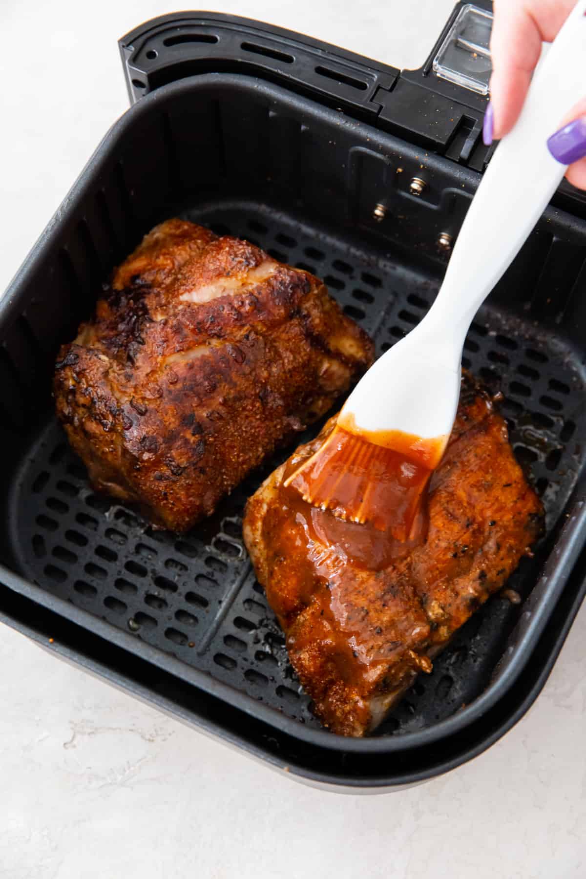 brushing bbq sauce onto cooked ribs in an air fryer basket