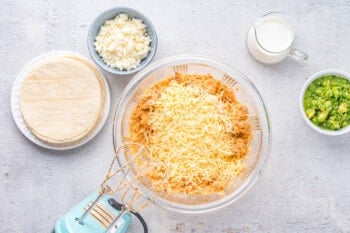 chicken taquito filling with shredded cheese in a glass bowl with a hand mixer