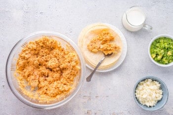 spoon spreading chicken taquito filling onto a corn tortilla