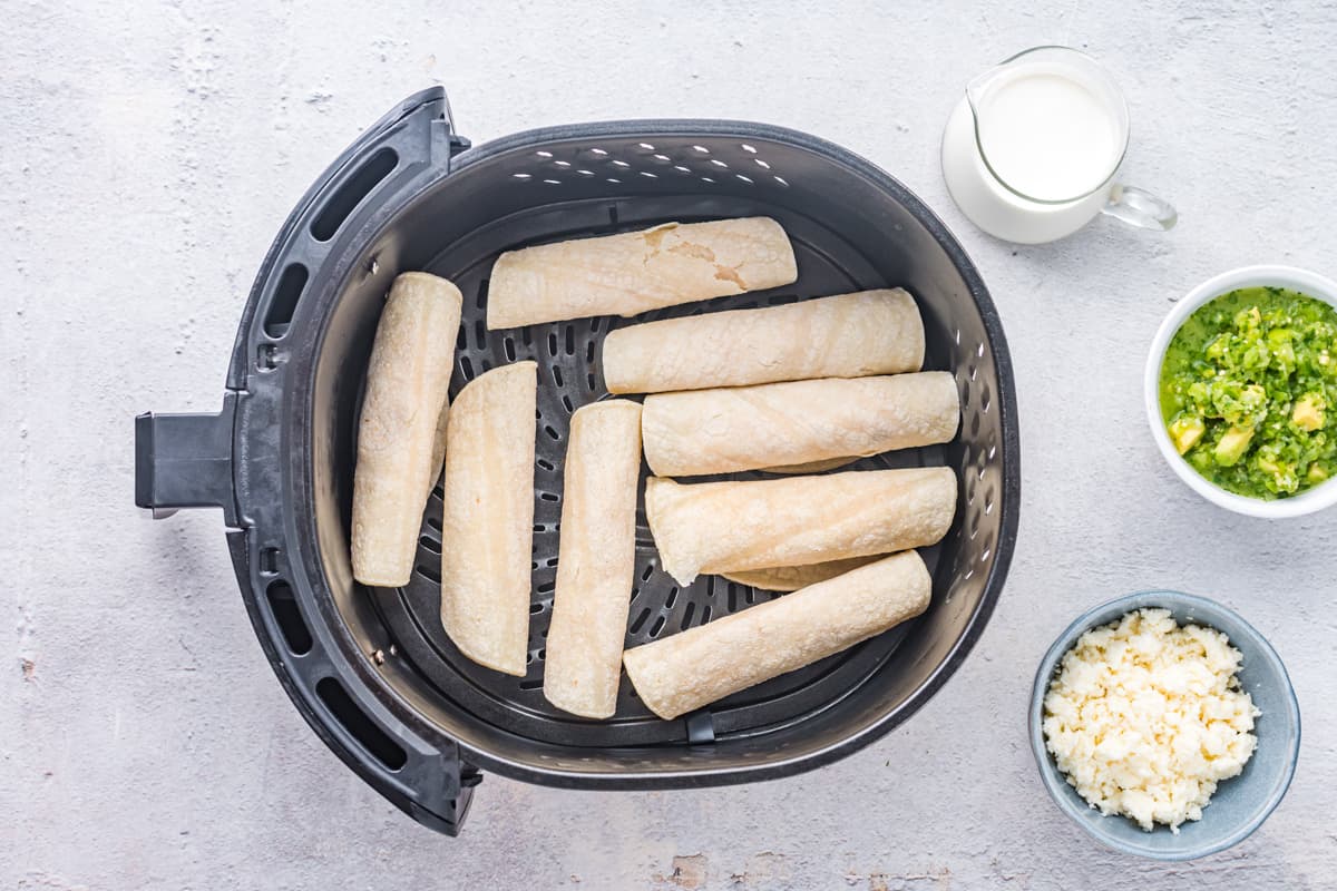 Chicken taquitos in air fryer basket before cooking.