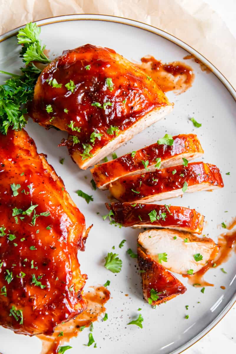 1 whole bbq chicken breast and 1 sliced bbq chicken breast on a white plate