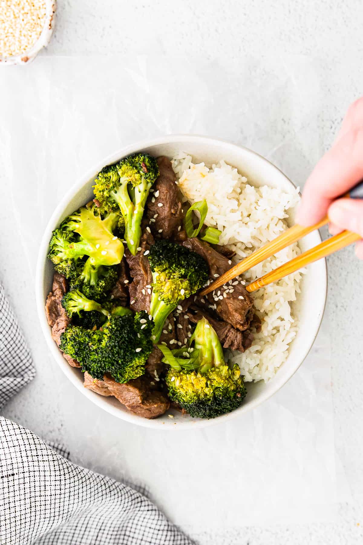 hands using chopsticks placed in a bowl of beef, broccoli, and rice