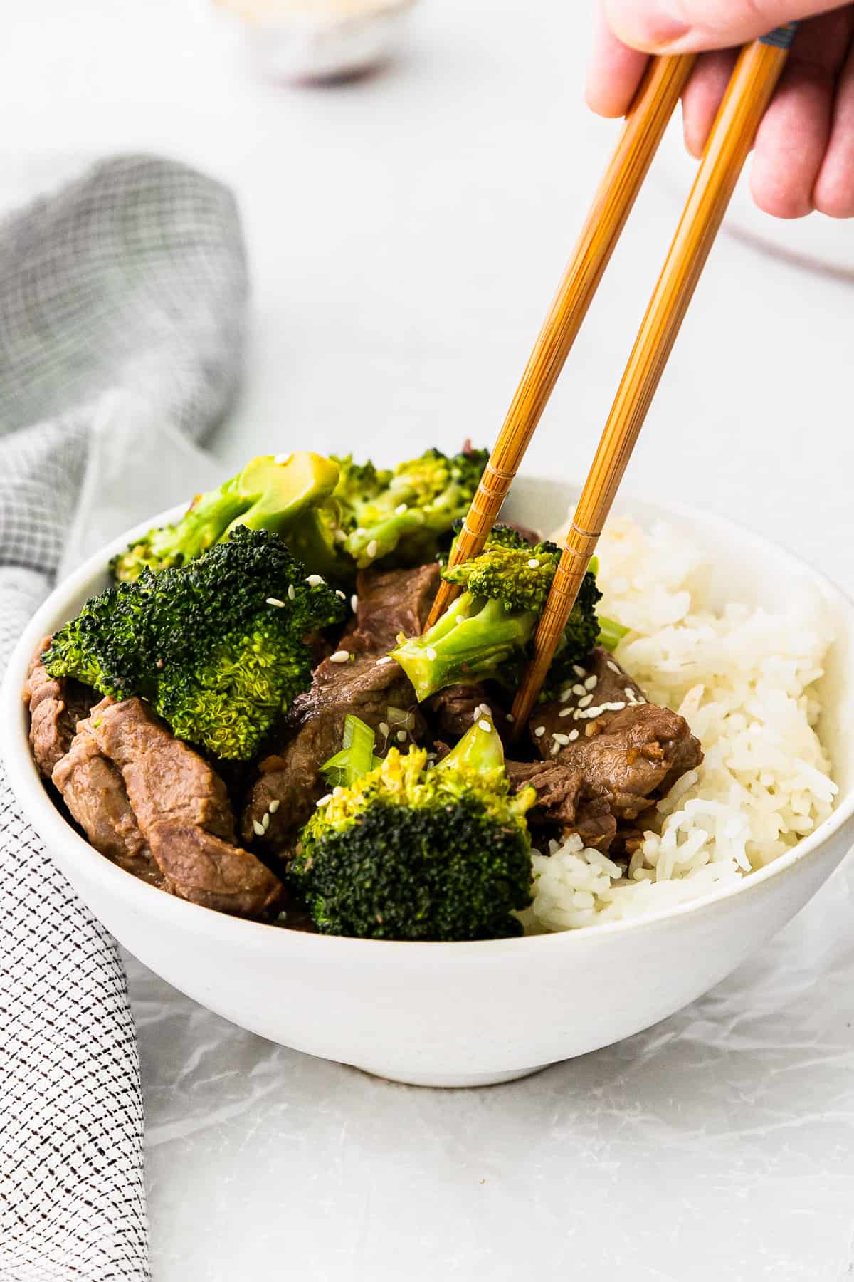 hands using chopsticks placed in a bowl of beef, broccoli, and rice