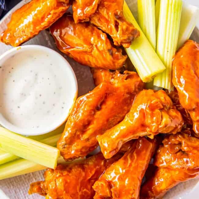overhead image of buffalo chicken wings, sliced carrots, sliced celery, and dressing in a white bowl on a white plate