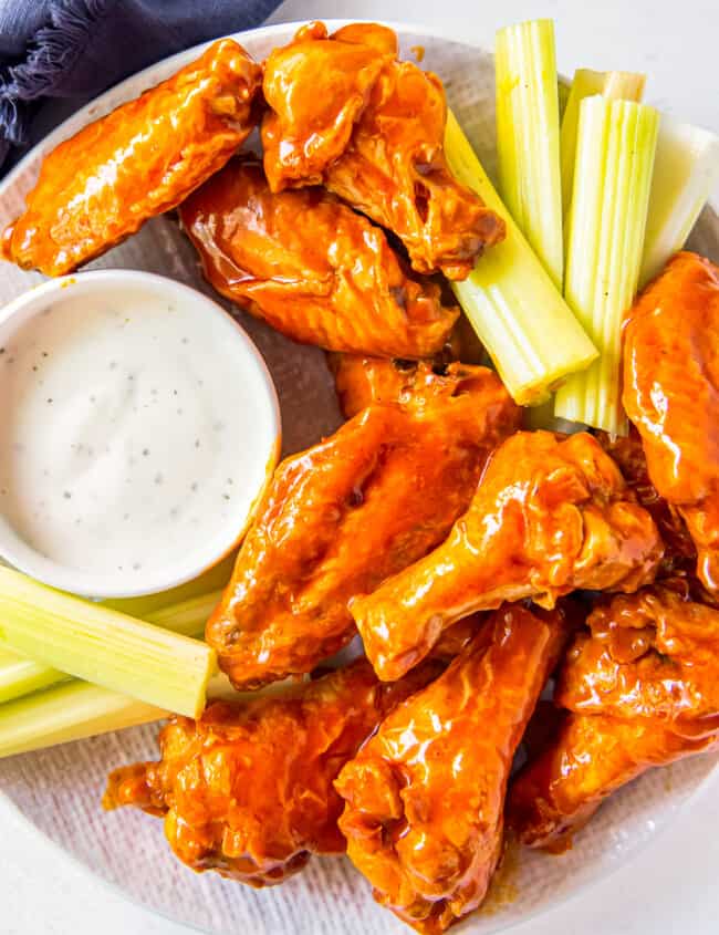 overhead image of buffalo chicken wings, sliced carrots, sliced celery, and dressing in a white bowl on a white plate