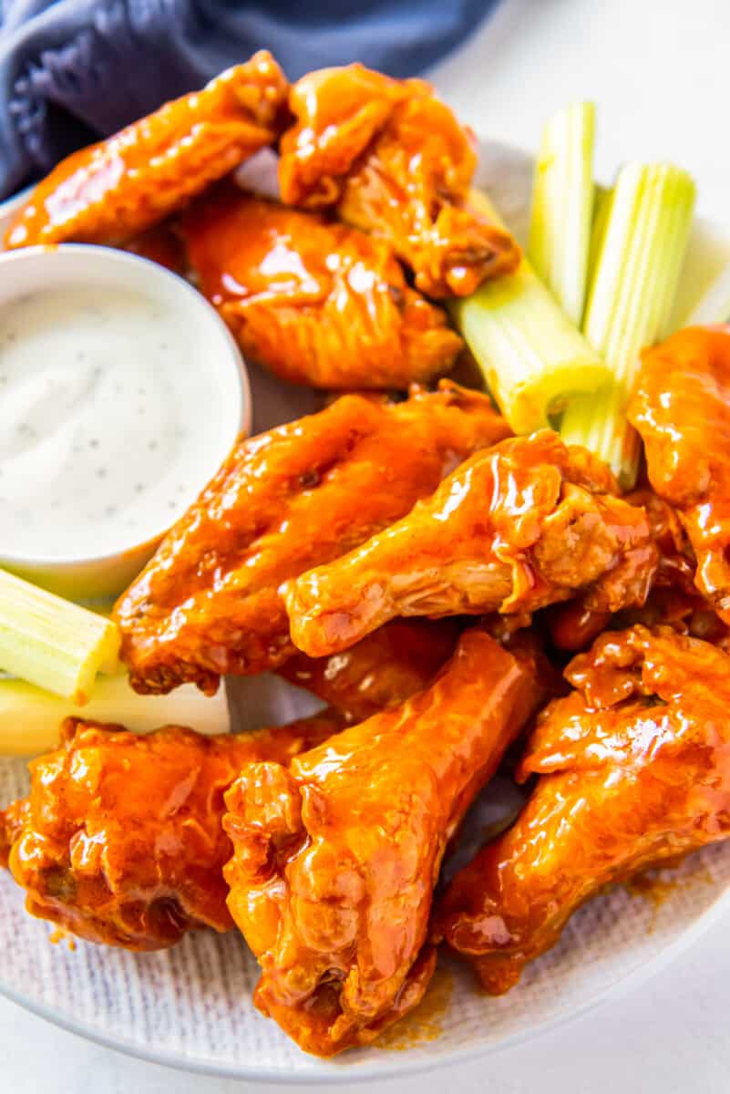 overhead image of buffalo chicken wings, sliced carrots, sliced celery, and dressing in a white bowl on a white plate