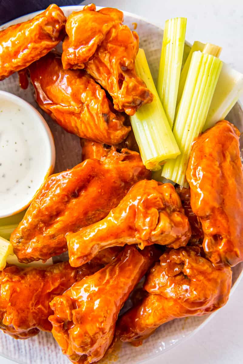 overhead image of buffalo chicken wings, sliced carrots, sliced celery, and dressing in a white bowl on a white plate