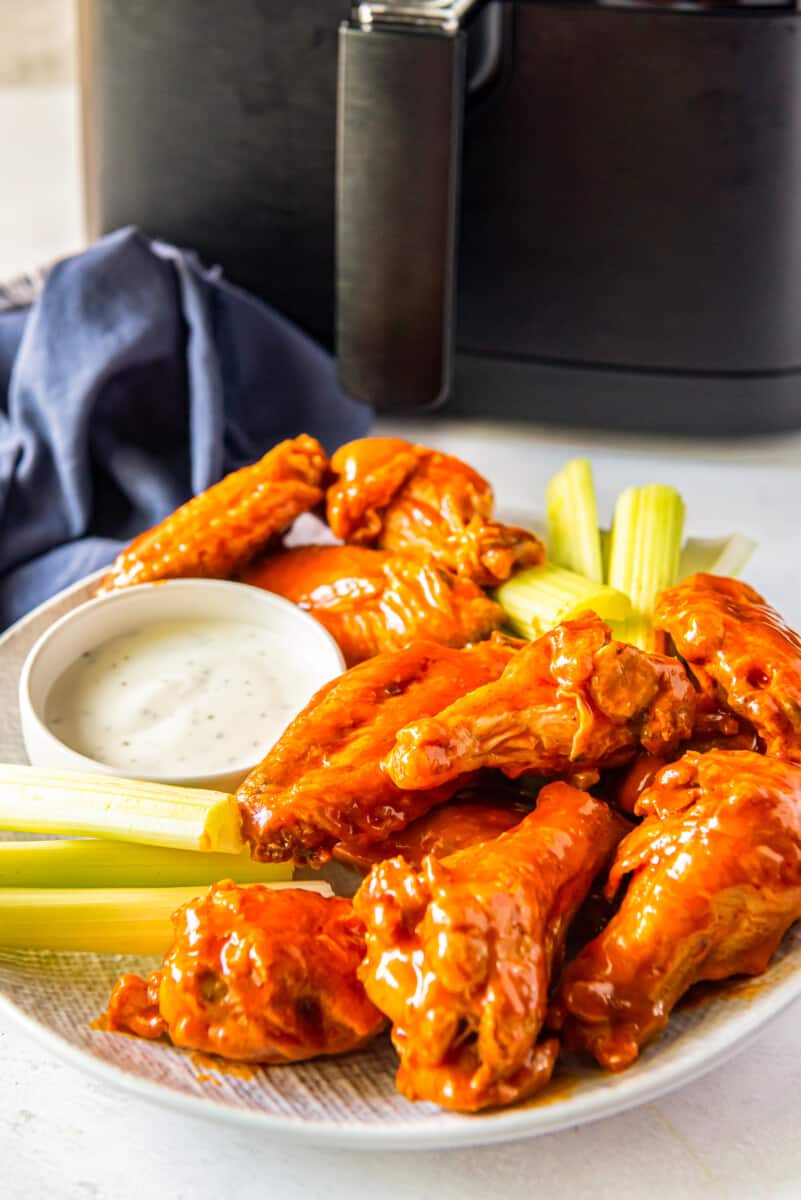 buffalo chicken wings, sliced carrots, sliced celery, and dressing in a white bowl on a white plate
