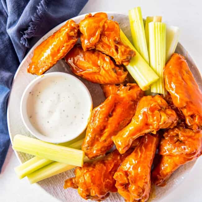 overhead image of buffalo chicken wings, sliced carrots, sliced celery, and dressing in a white bowl on a white plate