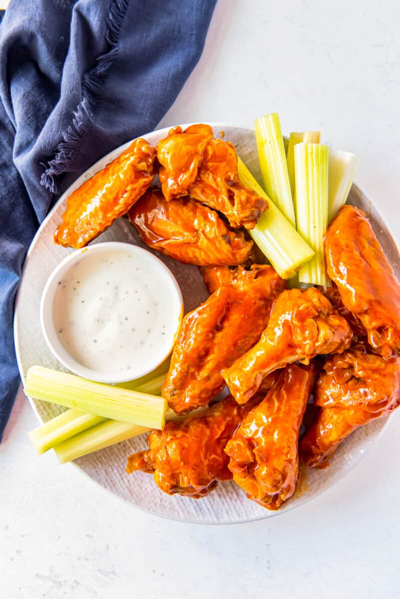 overhead image of buffalo chicken wings, sliced carrots, sliced celery, and dressing in a white bowl on a white plate