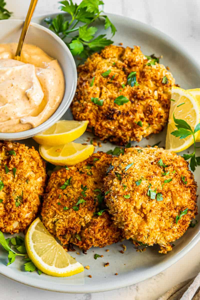 crab cakes on a plate with lemon slices and sauce in a bowl with a spoon