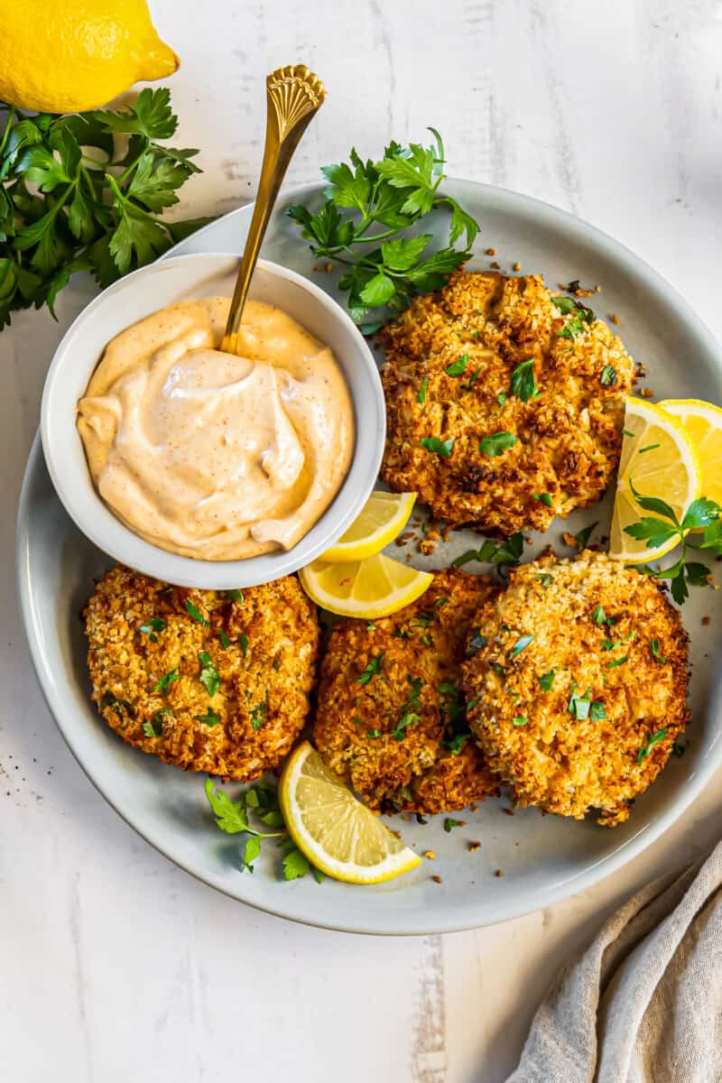 crab cakes on a plate with lemon slices and sauce in a bowl with a spoon