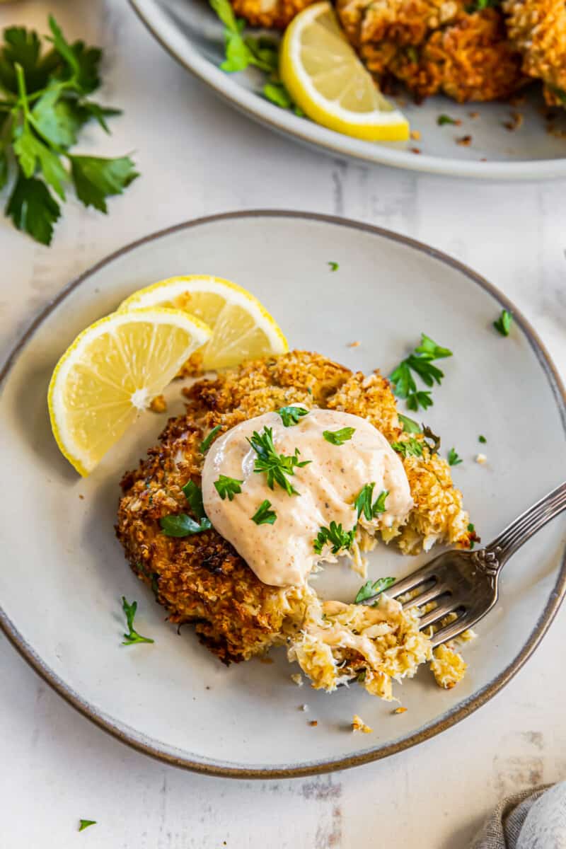 crab cake on a plate topped with sauce and garnished with lemon slices with a fork