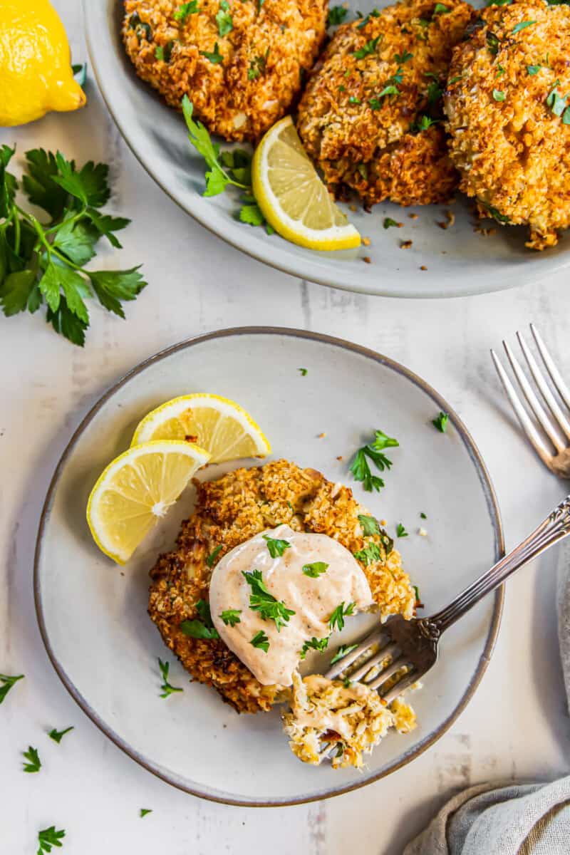 crab cake on a plate topped with sauce and garnished with lemon slices with a fork