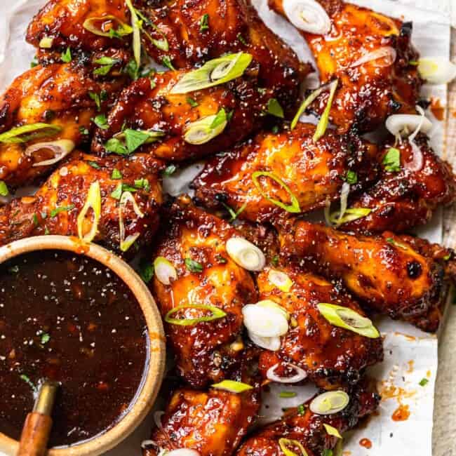baked korean hot wings on a serving platter with sauce in a bowl with a spoon