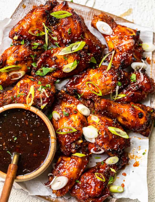 baked korean hot wings on a serving platter with sauce in a bowl with a spoon