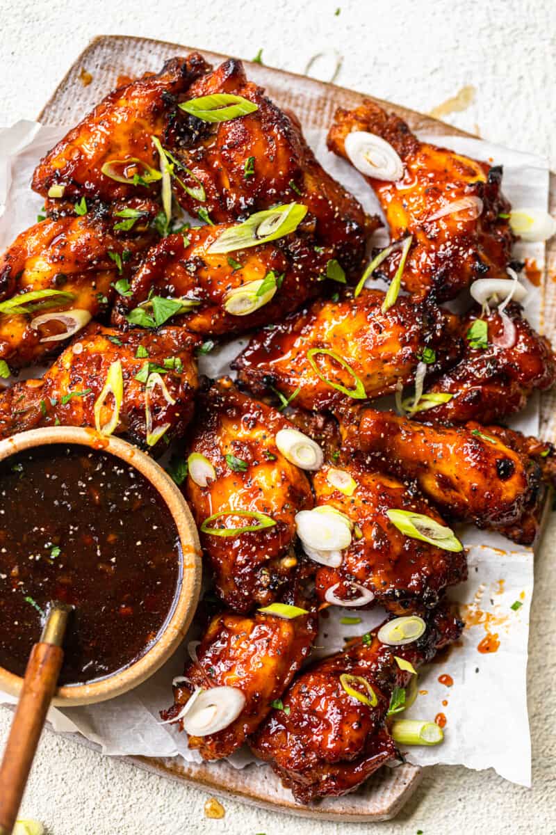 baked korean hot wings on a serving platter with sauce in a bowl with a spoon