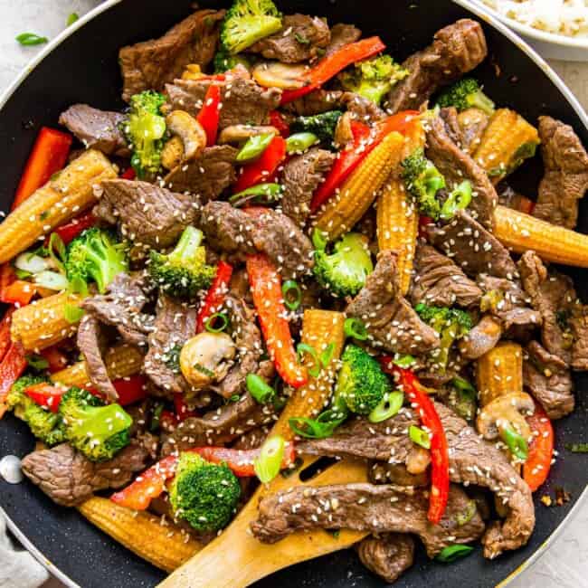 beef stir fry in a wok with a wood spoon