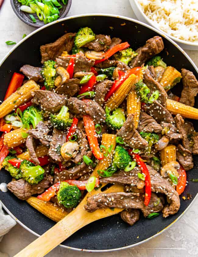 beef stir fry in a wok with a wood spoon