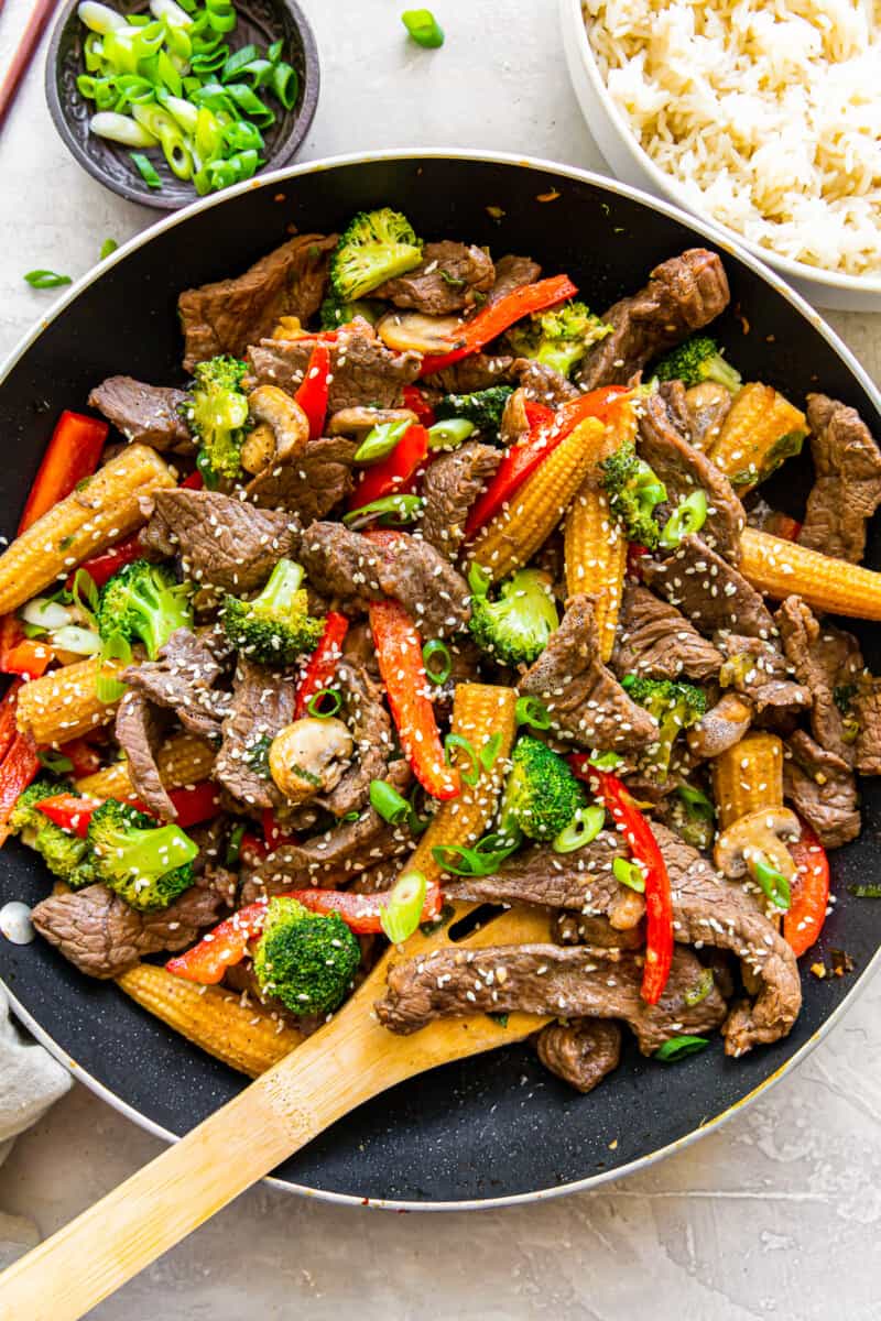 beef stir fry in a wok with a wood spoon