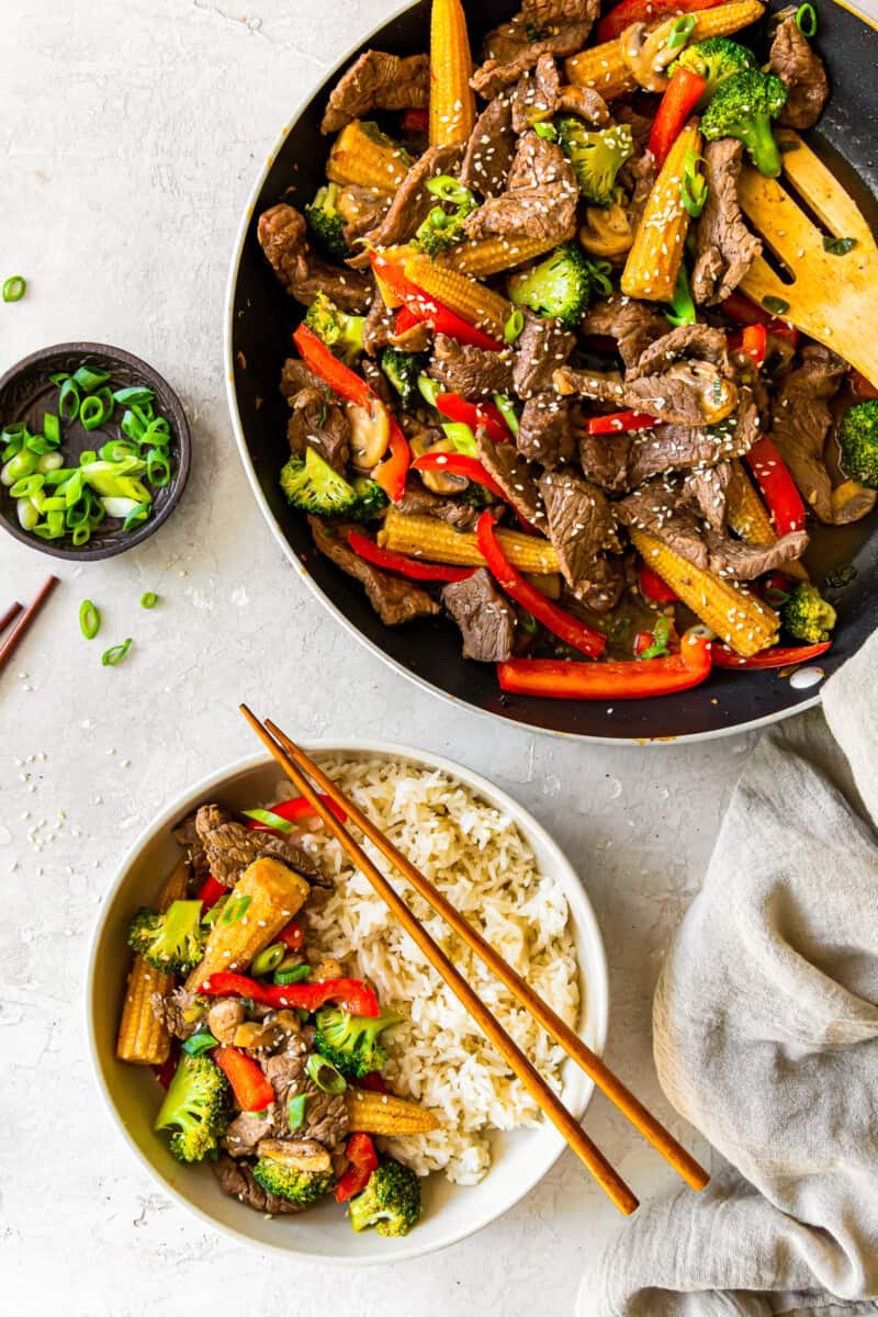 beef stir fry in a wok with a wood spoon and a serving of beef stir fry with rice in a white bowl with chopsticks