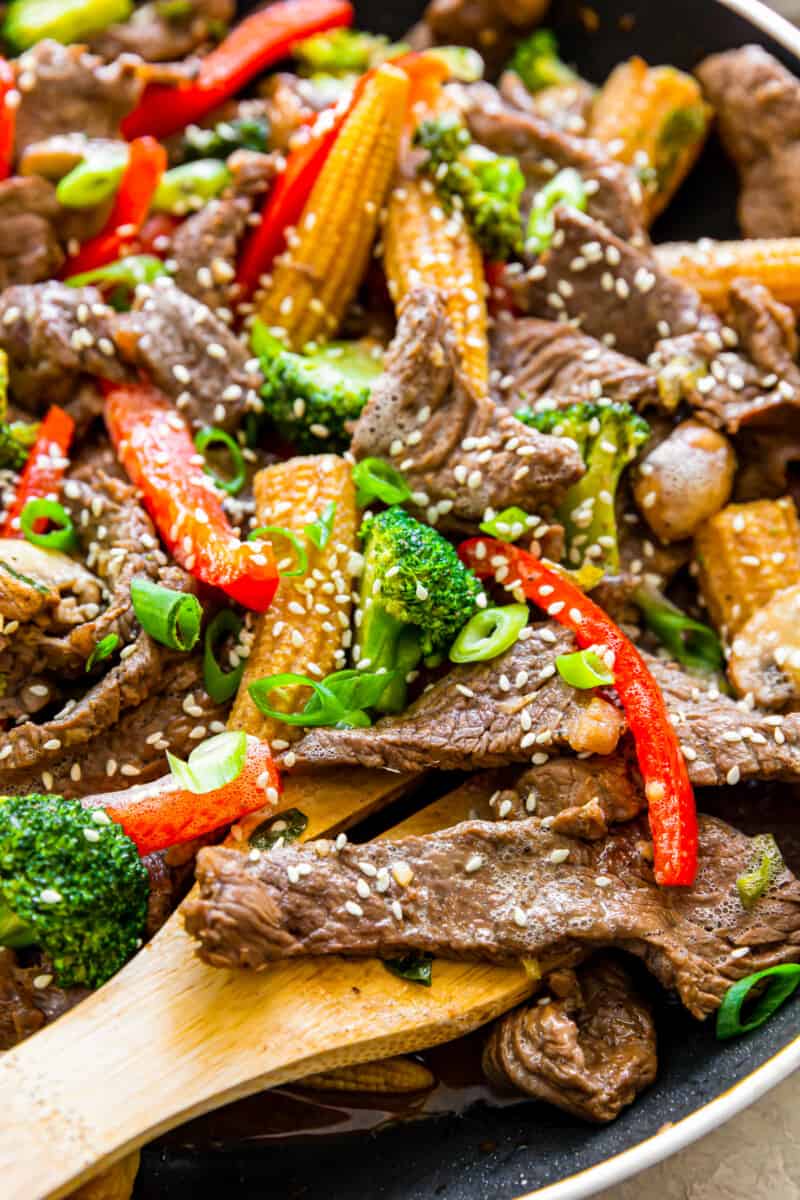 close up image of beef stir fry in a wok with a wood spoon