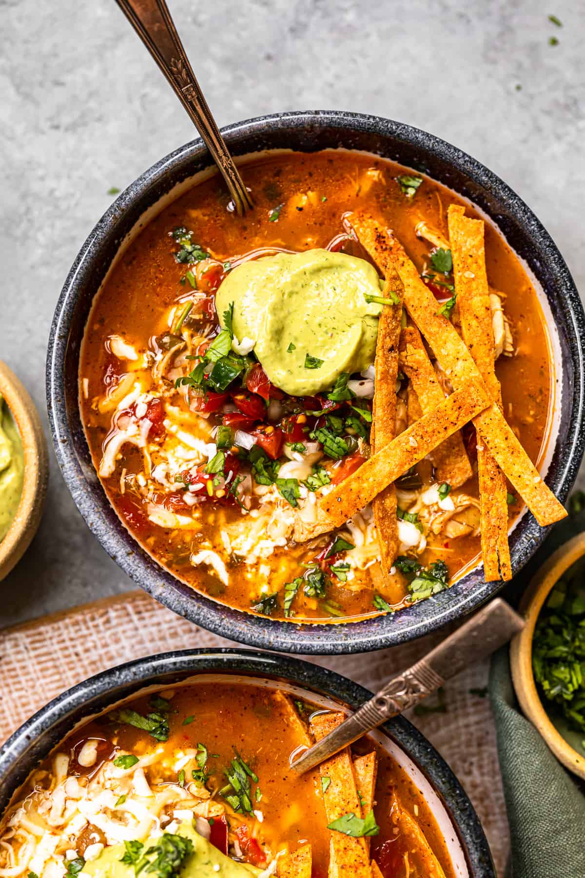 chicken fajita soup in a black bowl topped with cheese, guacamole, diced tomatoes, and tortilla strips with a spoon